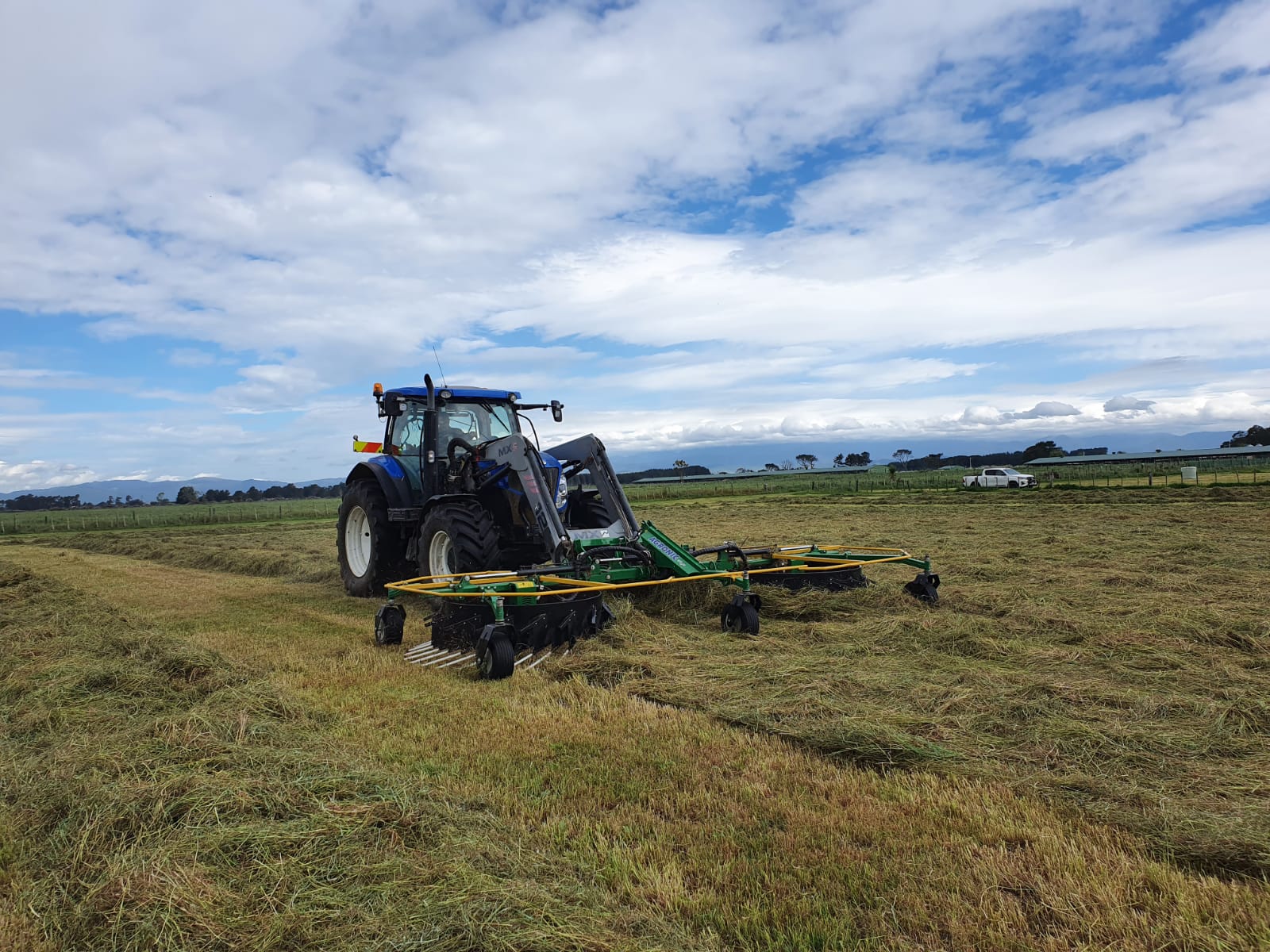 front mounted rake on tractor raking a row of hay